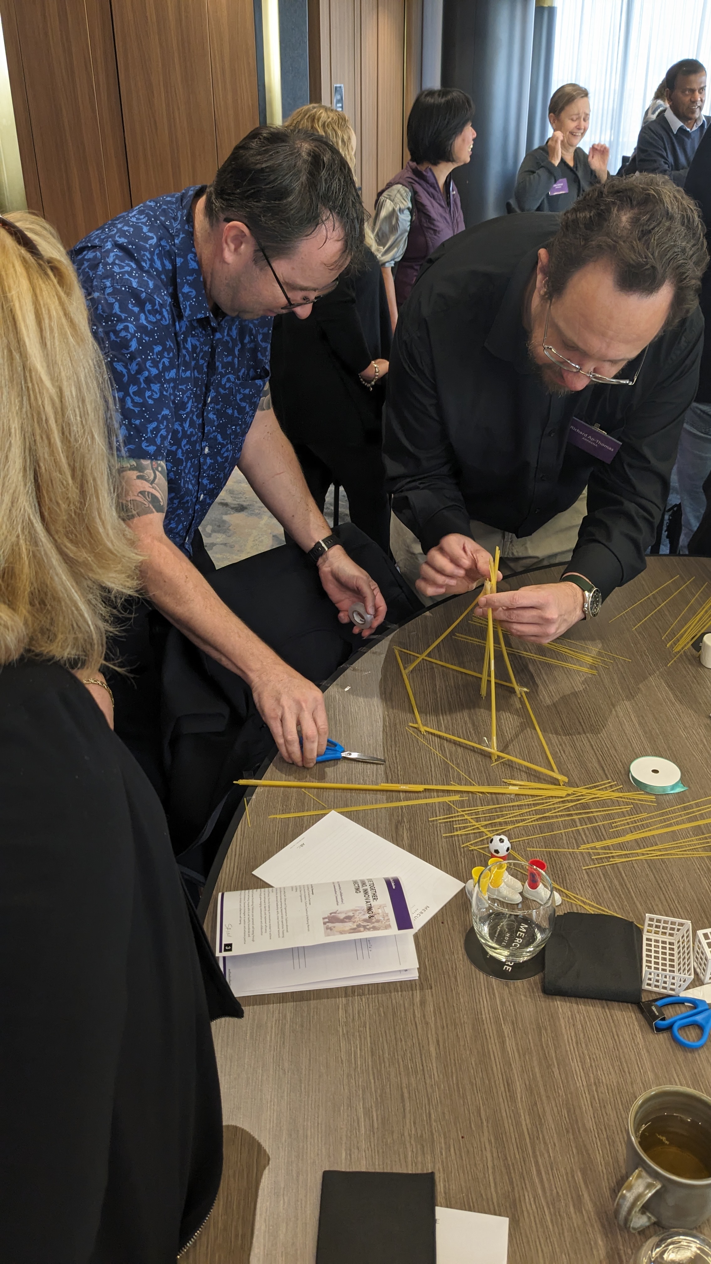 Workshop participants collaborate on a hands-on team activity, building a structure from uncooked spaghetti at a table.